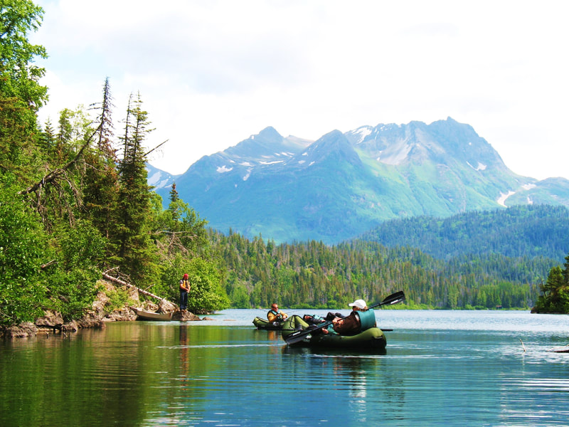 Several guests fishing from their kayaks and the shore of Leisure Lake with the mountains of the Kachemak Bay State Park in the background. 