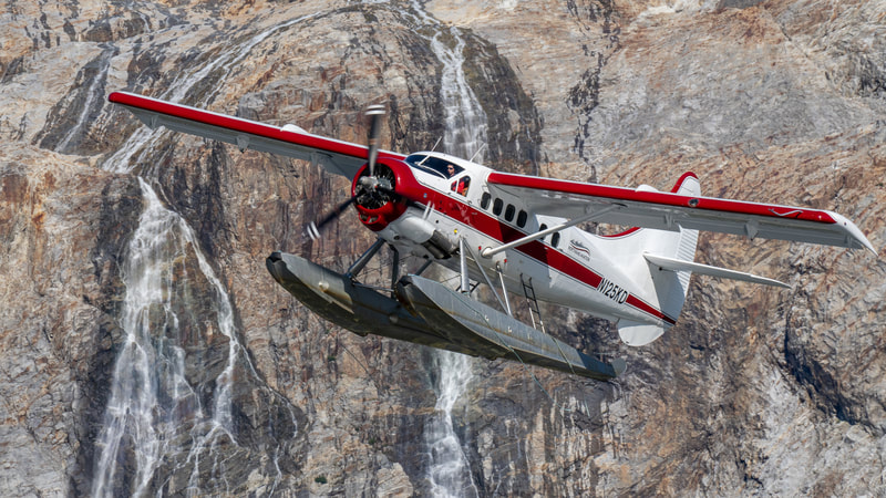 A beautiful red and white float plane taking off in front a waterfall. 