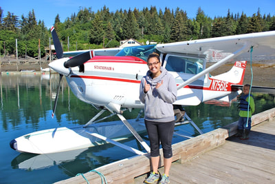 A very excited young woman posing in front of a float plane in the Halibut Cove Harbor. 