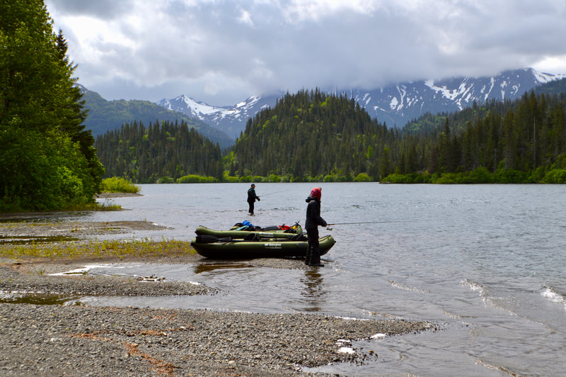 Two guests fishing next to their kayaks along the shore of Leisure Lake. 