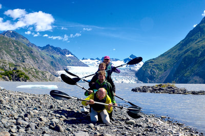 A family doing a goofy pose with their kayak paddles on the beach in front of the Grewingk Glacier Lake. 