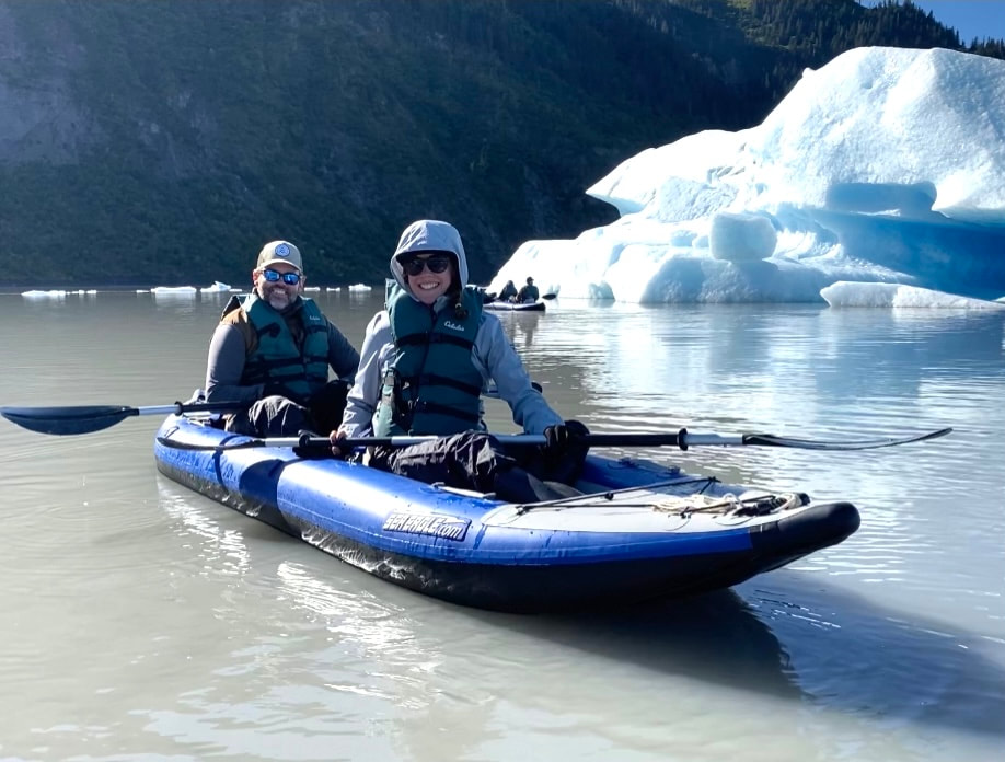 A couple posing in their inflatable kayak next to an iceberg on Grewingk Glacier Lake. 